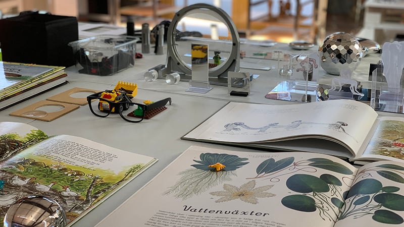 Ett bord med många prylar: Spegel, glasögon, lego, en bok.